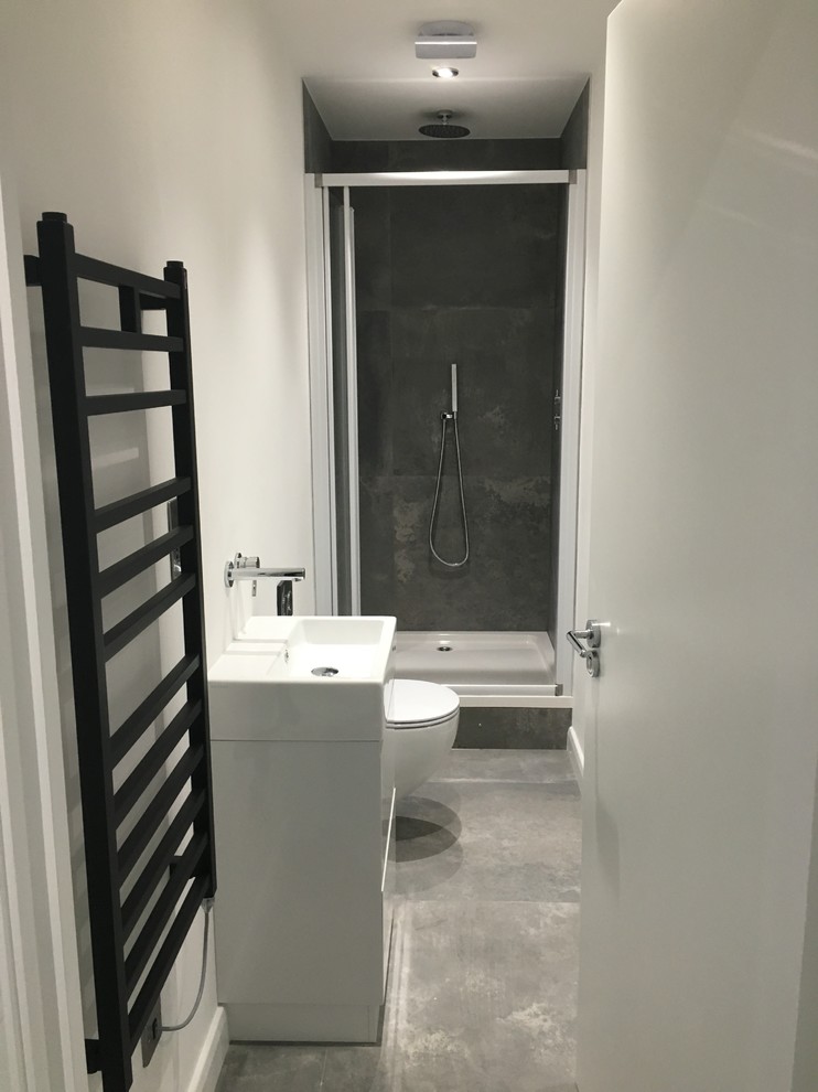 Photo of a large modern ensuite bathroom in London with freestanding cabinets, white cabinets, a freestanding bath, a double shower, a wall mounted toilet, grey tiles, ceramic tiles, white walls, ceramic flooring, an integrated sink and engineered stone worktops.