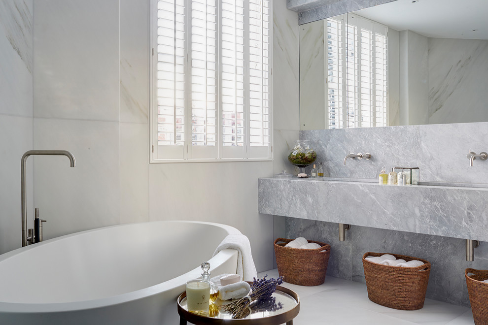 Réalisation d'une salle de bain design avec une baignoire indépendante, un mur blanc, un sol blanc et un plan de toilette gris.