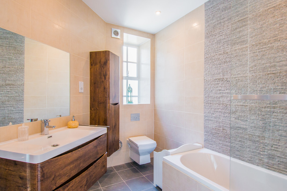 Bild på ett mellanstort funkis badrum, med släta luckor, bruna skåp, ett platsbyggt badkar, en vägghängd toalettstol och grått golv