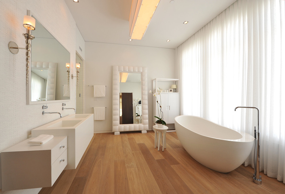 Modern inredning av ett stort en-suite badrum, med ett integrerad handfat, ett fristående badkar, släta luckor, vita skåp och vita väggar