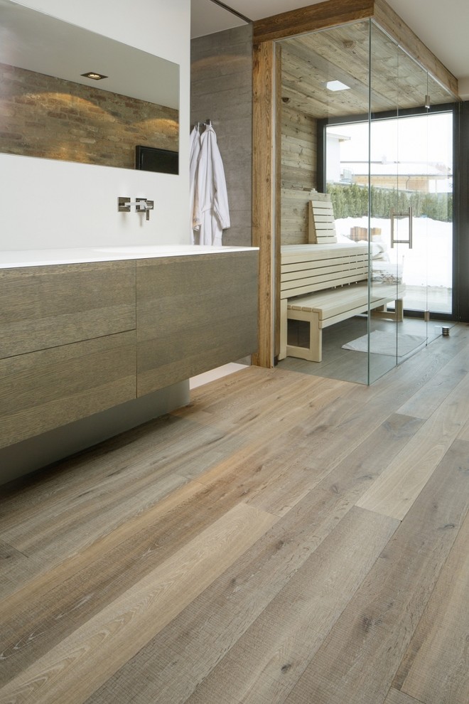 Modernes Badezimmer mit flächenbündigen Schrankfronten, hellbraunen Holzschränken, weißer Wandfarbe, braunem Holzboden und integriertem Waschbecken in Sonstige