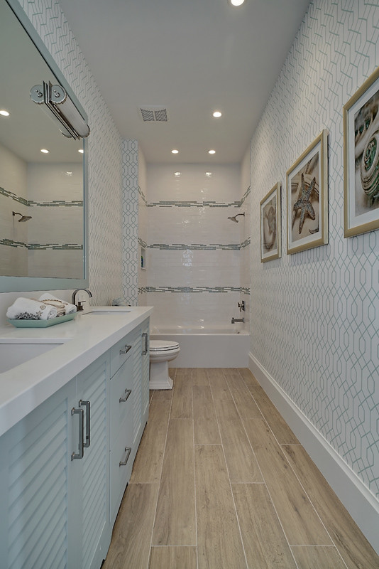 Inredning av ett maritimt stort vit vitt badrum, med luckor med lamellpanel, blå skåp, ett badkar i en alkov, en dusch/badkar-kombination, flerfärgad kakel, porslinskakel, flerfärgade väggar, mellanmörkt trägolv, ett undermonterad handfat, bänkskiva i kvartsit, brunt golv och dusch med duschdraperi