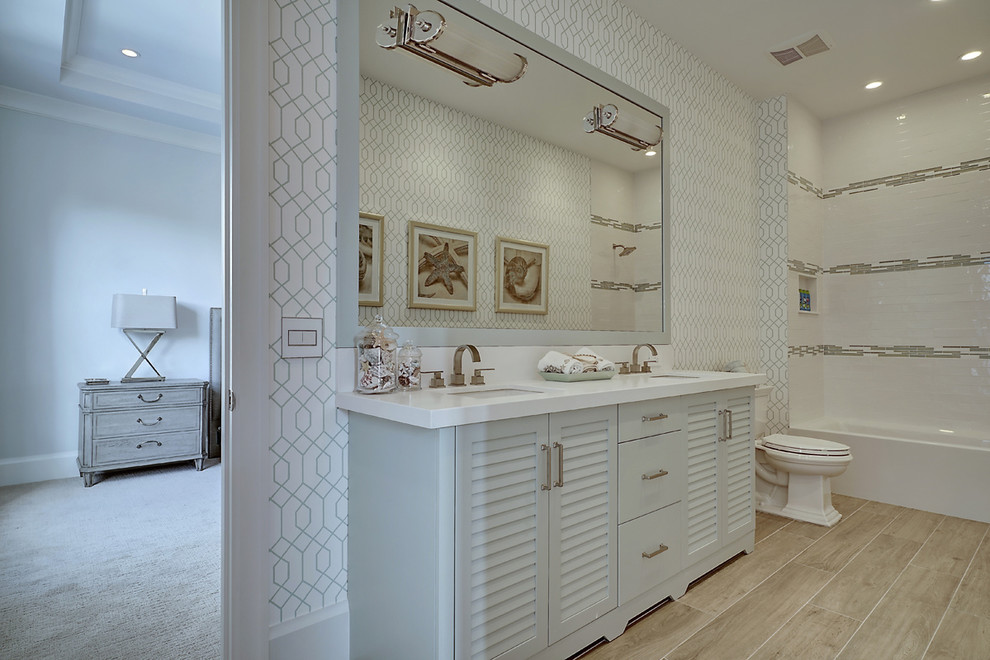 Klassisk inredning av ett stort en-suite badrum, med luckor med lamellpanel, ett badkar i en alkov, en dusch/badkar-kombination, en toalettstol med separat cisternkåpa, brun kakel, vit kakel, porslinskakel, vita väggar, ljust trägolv, ett undermonterad handfat, bänkskiva i kvartsit, blå skåp, brunt golv och dusch med duschdraperi