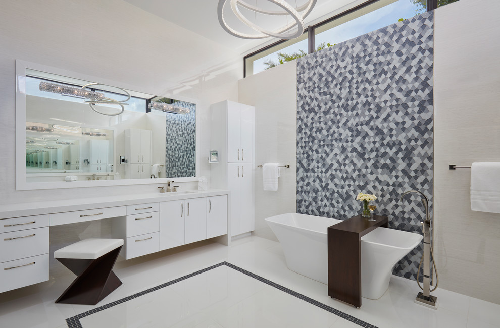 Modelo de cuarto de baño principal actual con armarios con paneles lisos, puertas de armario blancas, bañera exenta, baldosas y/o azulejos grises, paredes blancas y suelo blanco
