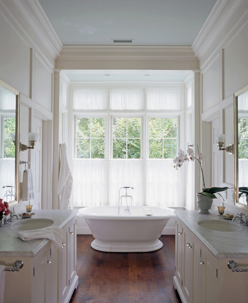 Foto de cuarto de baño tradicional con puertas de armario blancas, bañera exenta, paredes grises, suelo de madera oscura y lavabo bajoencimera