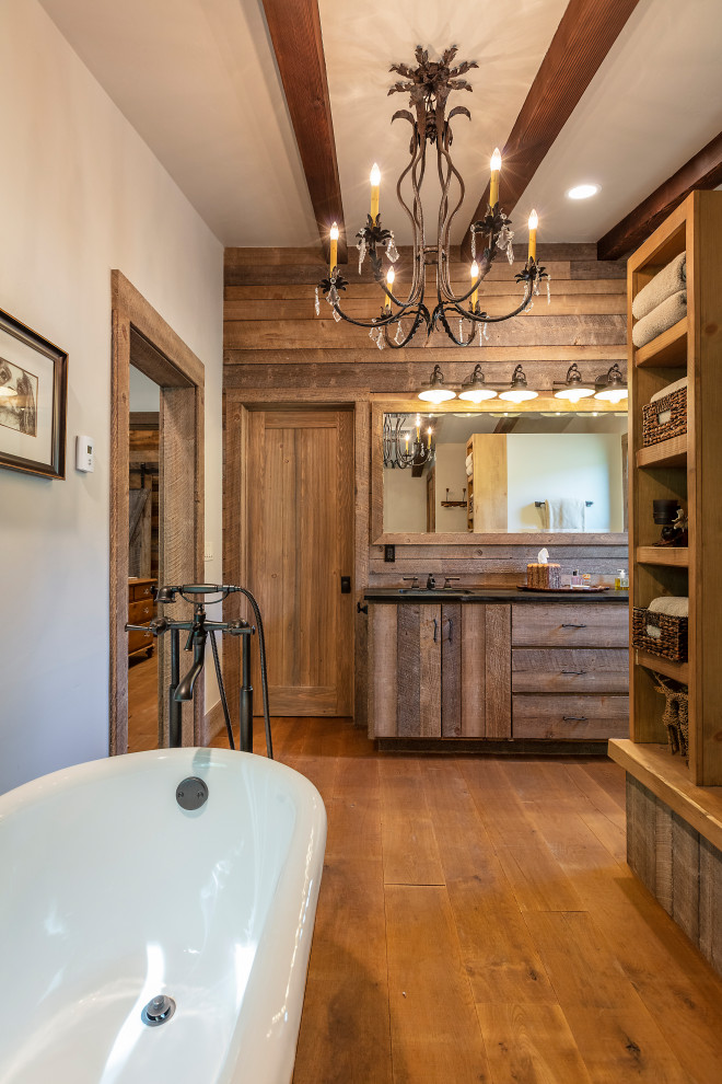 This is an example of a rustic bathroom in Denver with flat-panel cabinets, medium wood cabinets, a freestanding bath, white walls, medium hardwood flooring, a submerged sink, brown floors, black worktops, double sinks and a built in vanity unit.