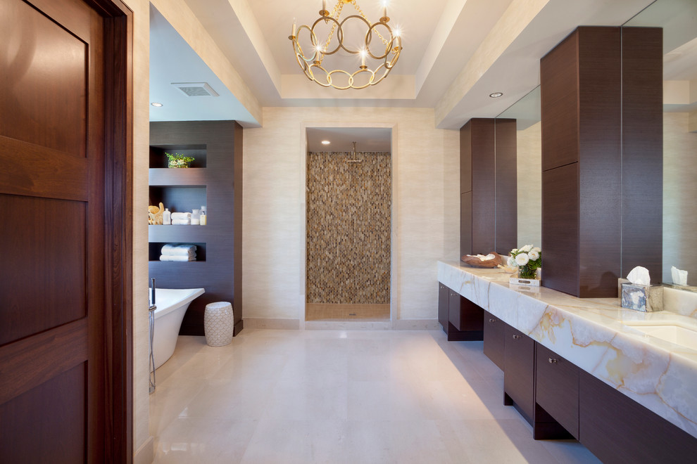 Cette photo montre une grande douche en alcôve principale chic en bois foncé avec un lavabo encastré, un placard à porte plane, un plan de toilette en marbre, une baignoire indépendante, un mur beige et un sol beige.