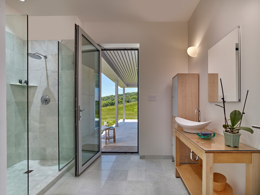 Inredning av ett modernt stort badrum med dusch, med skåp i ljust trä, ett fristående badkar, en hörndusch, vit kakel, vita väggar, klinkergolv i porslin, möbel-liknande, ett fristående handfat, bänkskiva i glas, vitt golv, med dusch som är öppen och marmorkakel