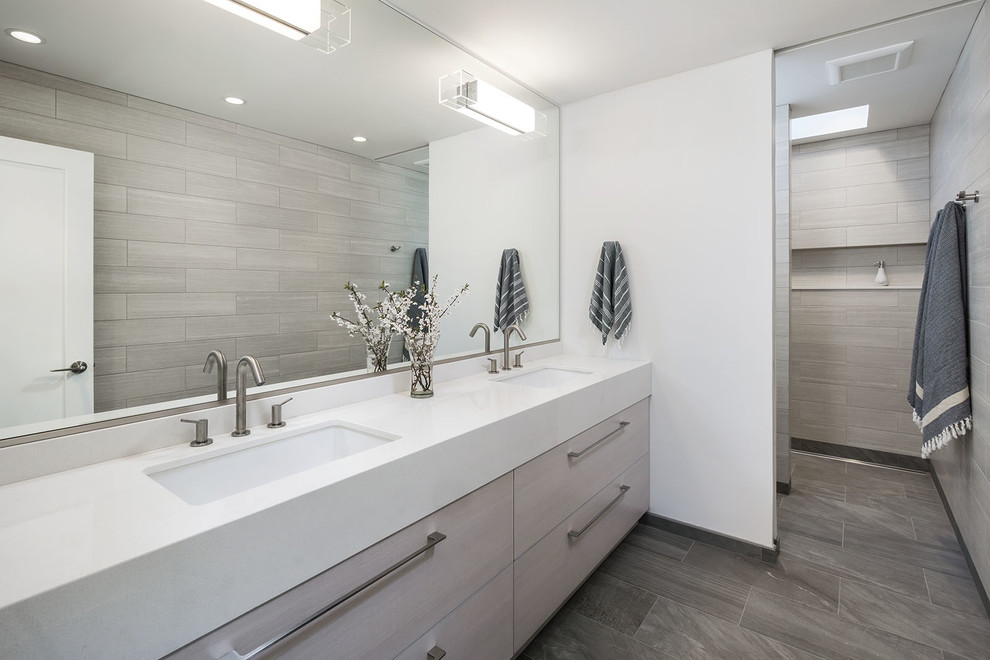 Foto de cuarto de baño nórdico con lavabo bajoencimera, armarios con paneles lisos, puertas de armario de madera clara, baldosas y/o azulejos grises y paredes blancas