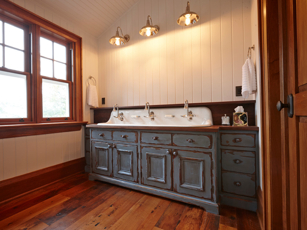 Rustik inredning av ett mellanstort badrum för barn, med ett avlångt handfat, möbel-liknande, skåp i slitet trä, träbänkskiva, vita väggar och mörkt trägolv
