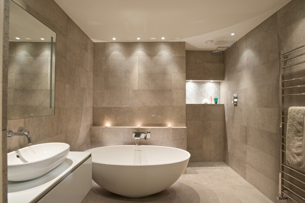 ロンドンにあるコンテンポラリースタイルのおしゃれな浴室 (ベッセル式洗面器、フラットパネル扉のキャビネット、白いキャビネット、置き型浴槽、ベージュのタイル、ベージュの壁、バリアフリー、照明) の写真