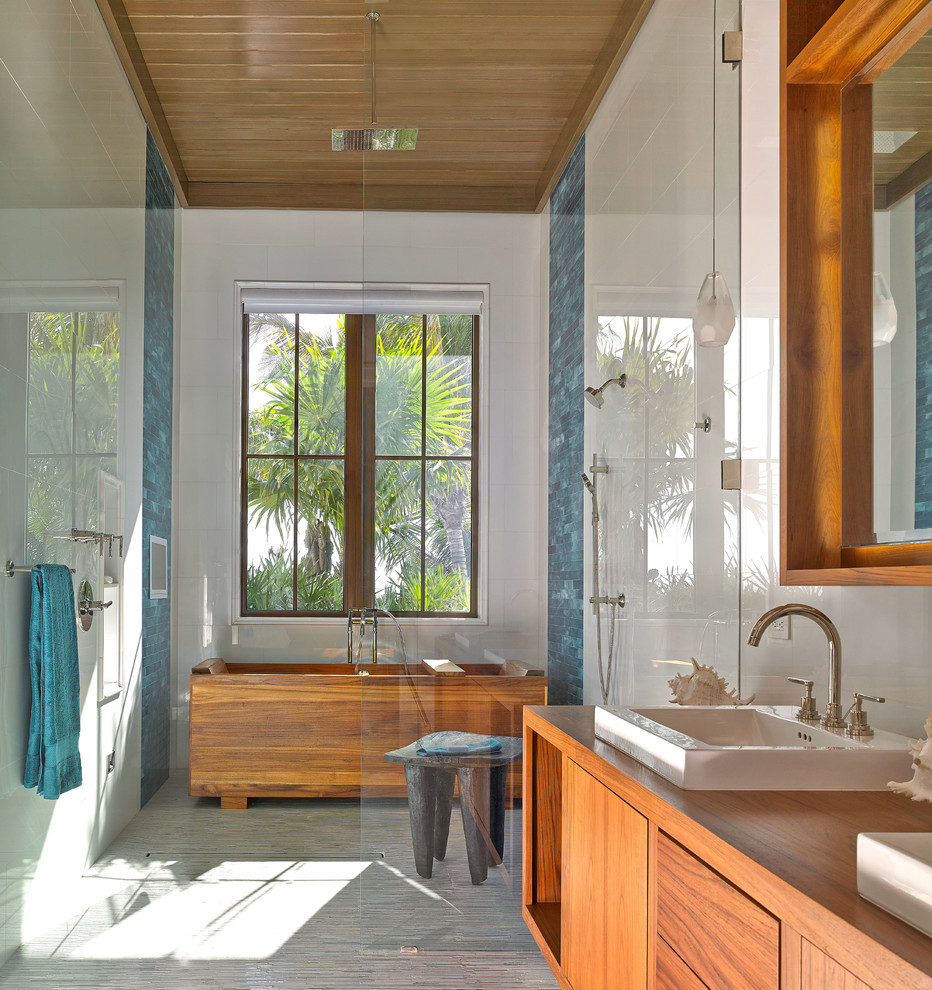 マイアミにあるトロピカルスタイルのおしゃれな浴室 (フラットパネル扉のキャビネット、ベッセル式洗面器、中間色木目調キャビネット、木製洗面台、置き型浴槽、アルコーブ型シャワー、青いタイル、ブラウンの洗面カウンター) の写真