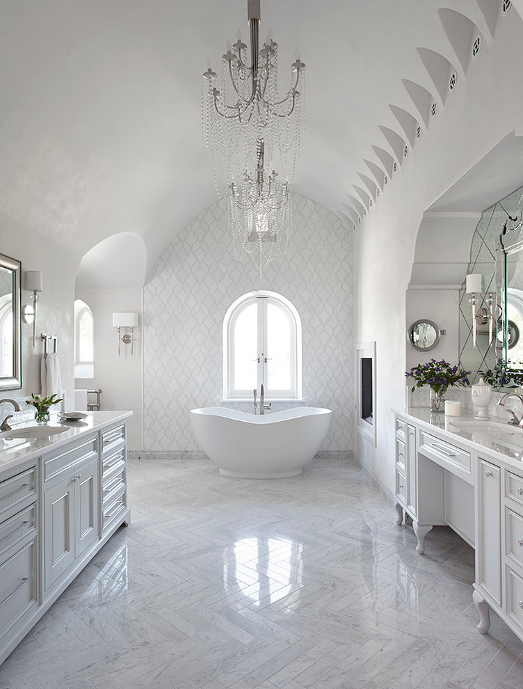 オースティンにある地中海スタイルのおしゃれなマスターバスルーム (落し込みパネル扉のキャビネット、白いキャビネット、置き型浴槽、白いタイル、白い壁、アンダーカウンター洗面器) の写真