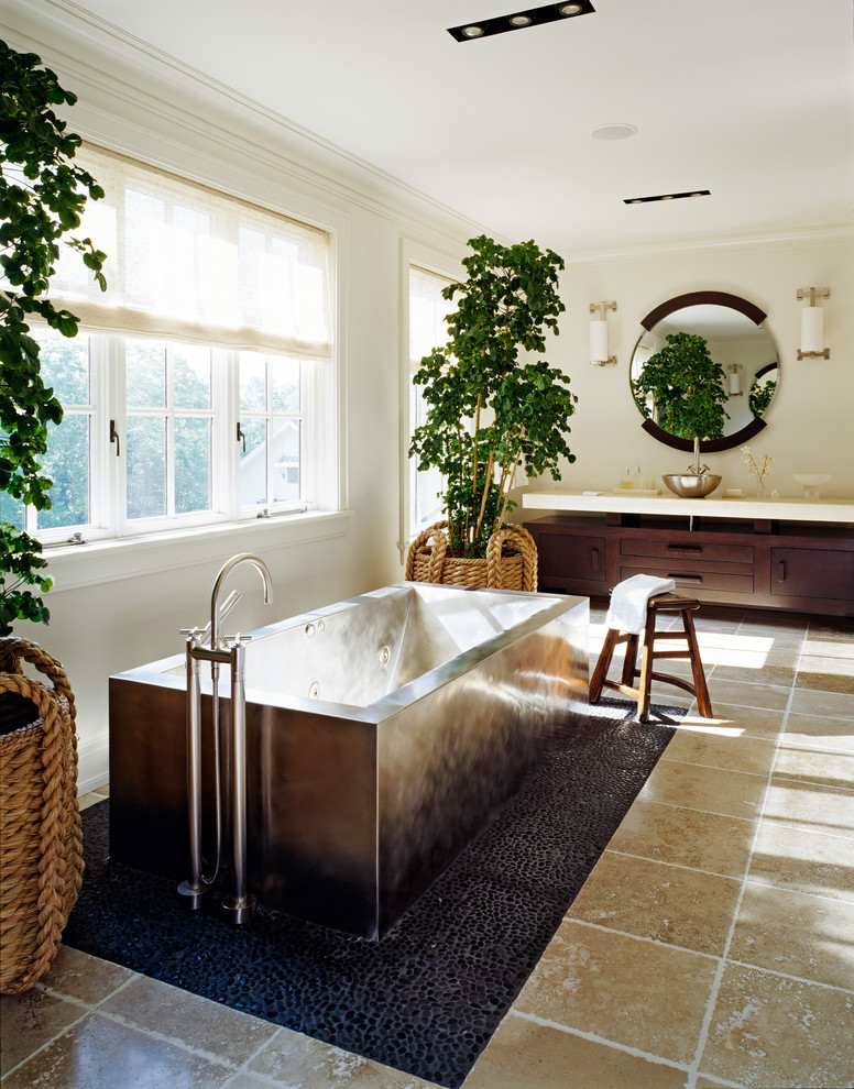 Réalisation d'une salle de bain principale design en bois foncé avec une baignoire indépendante, une vasque, un sol en galet, un plan de toilette en surface solide, un carrelage beige, des carreaux de céramique, un mur blanc et un placard à porte plane.