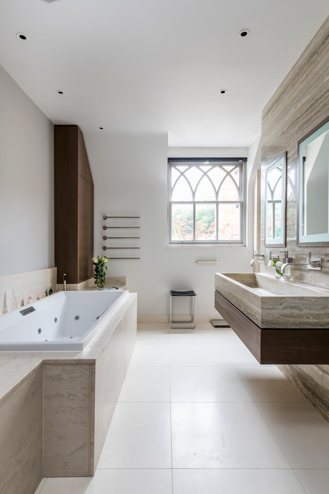 ウィルトシャーにあるコンテンポラリースタイルのおしゃれなマスターバスルーム (ライムストーンの床、ドロップイン型浴槽、石タイル、白い壁、横長型シンク) の写真
