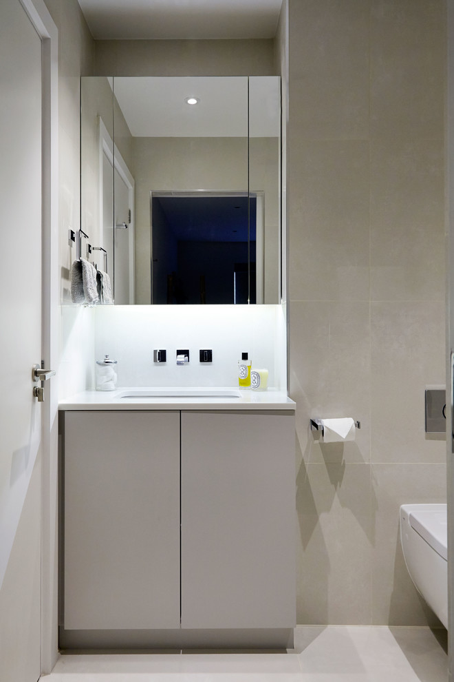 This is an example of a contemporary ensuite bathroom in London with flat-panel cabinets, a built-in bath, a wall mounted toilet, beige tiles, ceramic tiles, beige walls, ceramic flooring, a submerged sink and solid surface worktops.