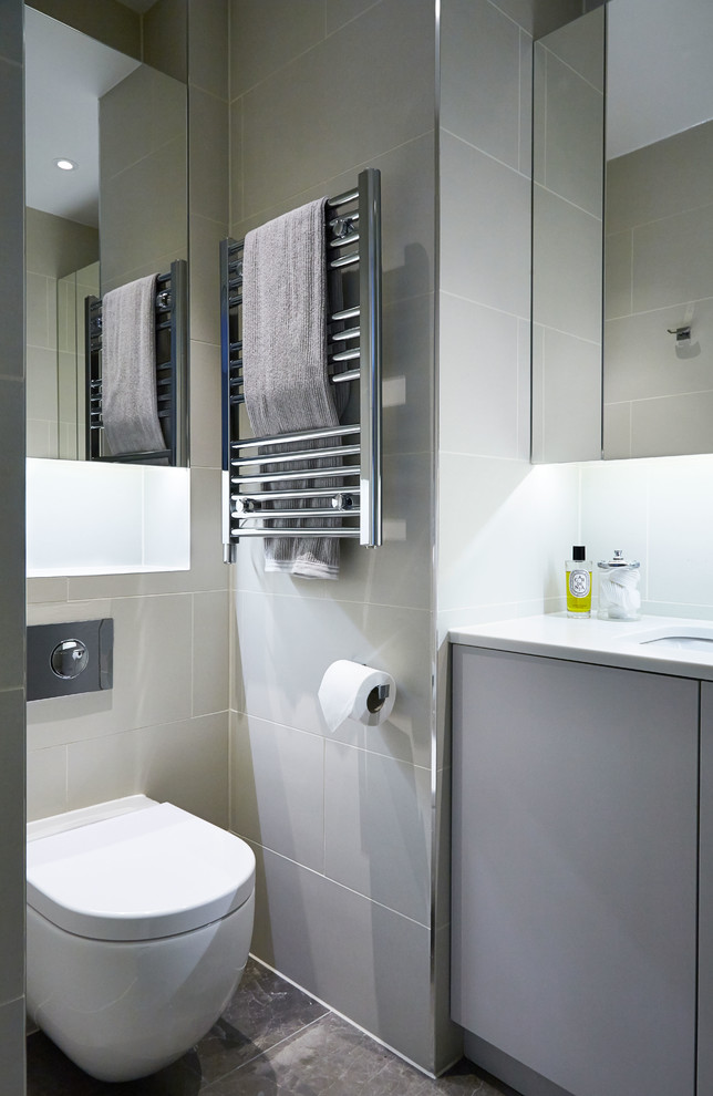 Photo of a contemporary ensuite bathroom in London with flat-panel cabinets, a built-in shower, a wall mounted toilet, beige tiles, ceramic tiles, beige walls, marble flooring, a submerged sink and solid surface worktops.