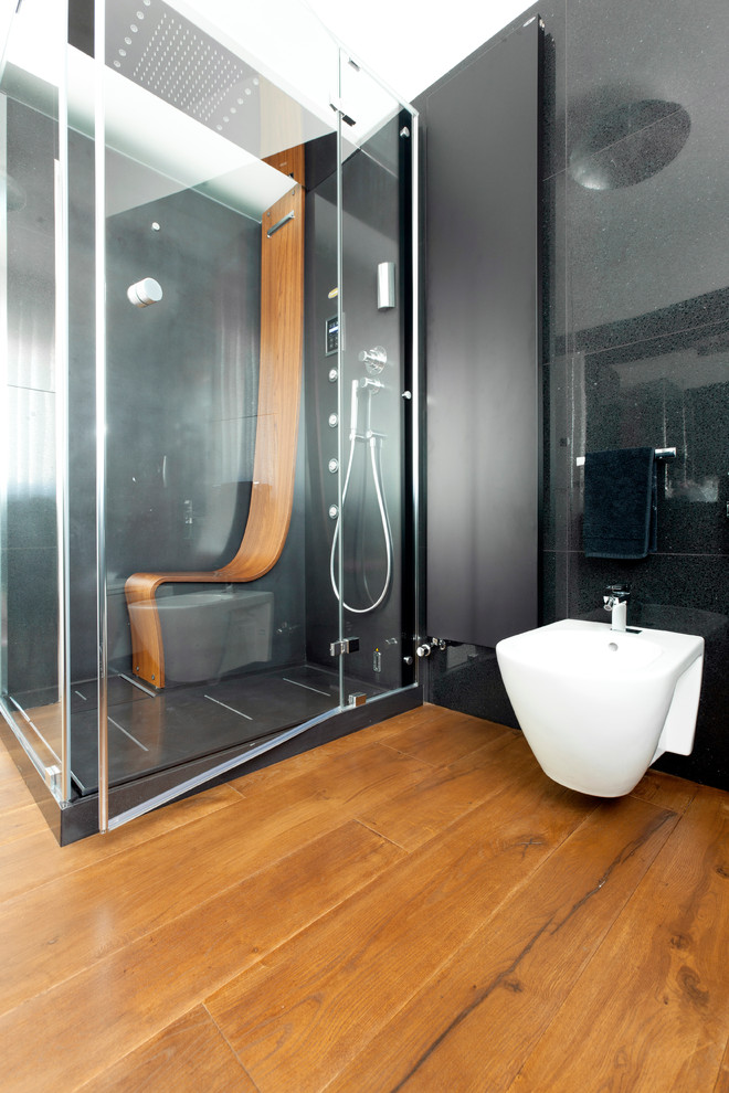 Exemple d'une salle de bain tendance avec une douche d'angle, WC suspendus, un carrelage noir, un mur noir et un sol en bois brun.