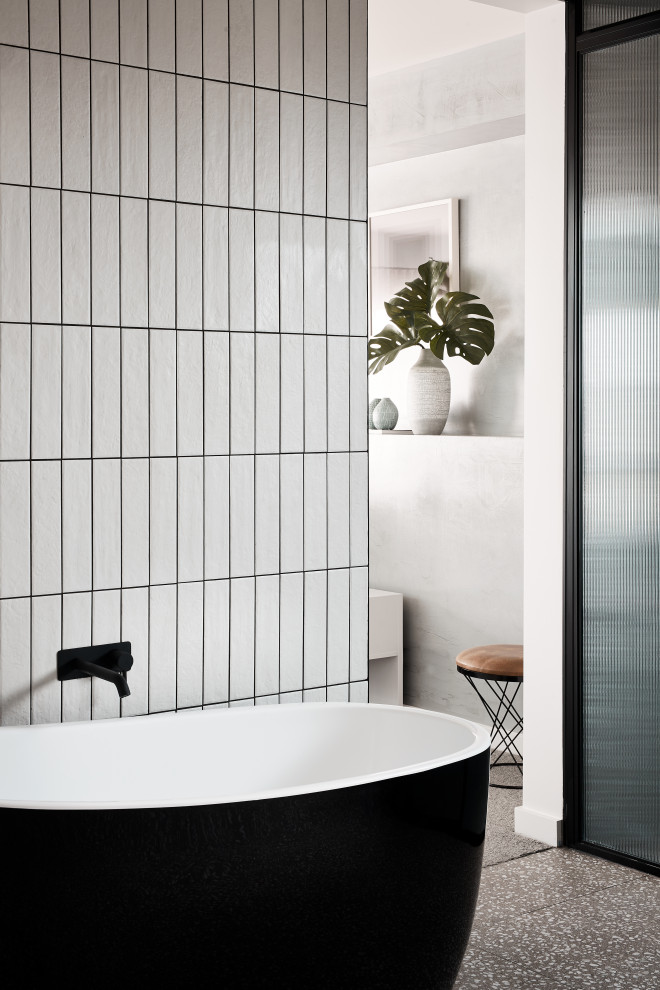 Imagen de cuarto de baño actual con bañera exenta, baldosas y/o azulejos blancos, baldosas y/o azulejos de cemento, paredes blancas, suelo de terrazo y suelo gris