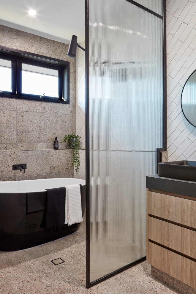 Photo of a contemporary ensuite wet room bathroom in Melbourne with flat-panel cabinets, medium wood cabinets, a freestanding bath, white tiles, metro tiles, terrazzo flooring, a vessel sink, brown floors and black worktops.