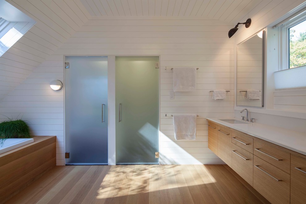 Immagine di una stanza da bagno contemporanea con ante lisce, ante in legno scuro, vasca da incasso, pareti bianche, parquet chiaro e lavabo integrato