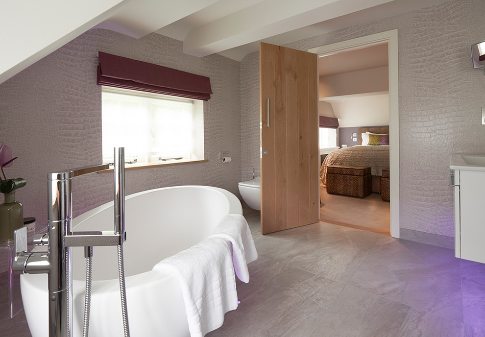 Inspiration for a medium sized contemporary ensuite bathroom in Berkshire with flat-panel cabinets, white cabinets, a freestanding bath, a wall mounted toilet, grey walls, a wall-mounted sink and grey floors.