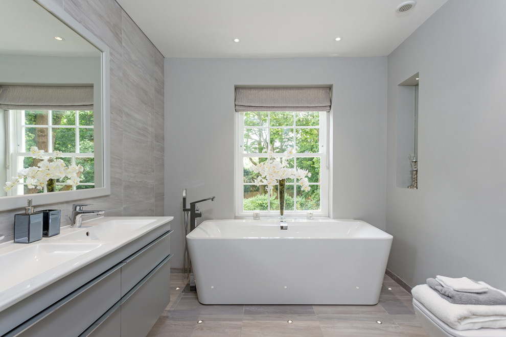 Imagen de cuarto de baño contemporáneo de tamaño medio con bañera exenta, paredes grises y suelo gris