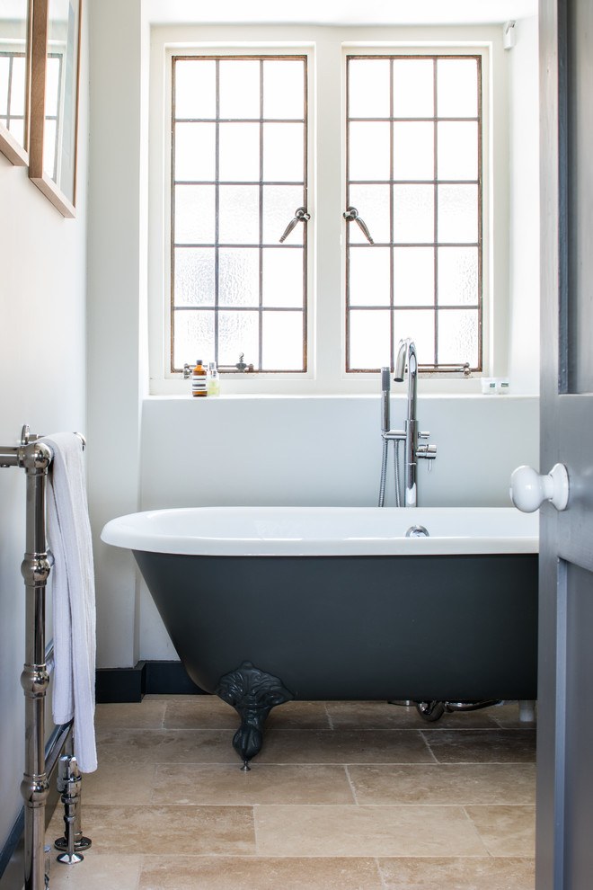 Foto på ett badrum, med ett badkar med tassar, kalkstensgolv och beiget golv