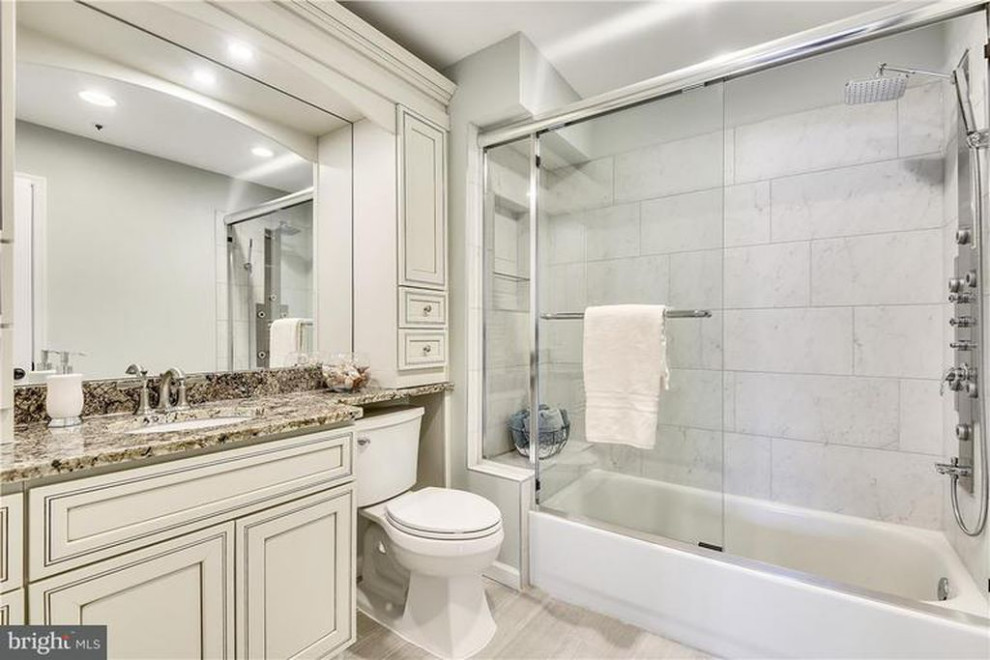 This is an example of a medium sized contemporary ensuite bathroom in DC Metro with recessed-panel cabinets, grey cabinets, an alcove bath, an alcove shower, a two-piece toilet, grey tiles, ceramic tiles, grey walls, ceramic flooring, a submerged sink, granite worktops, grey floors, a sliding door, multi-coloured worktops, a wall niche, a single sink and a built in vanity unit.