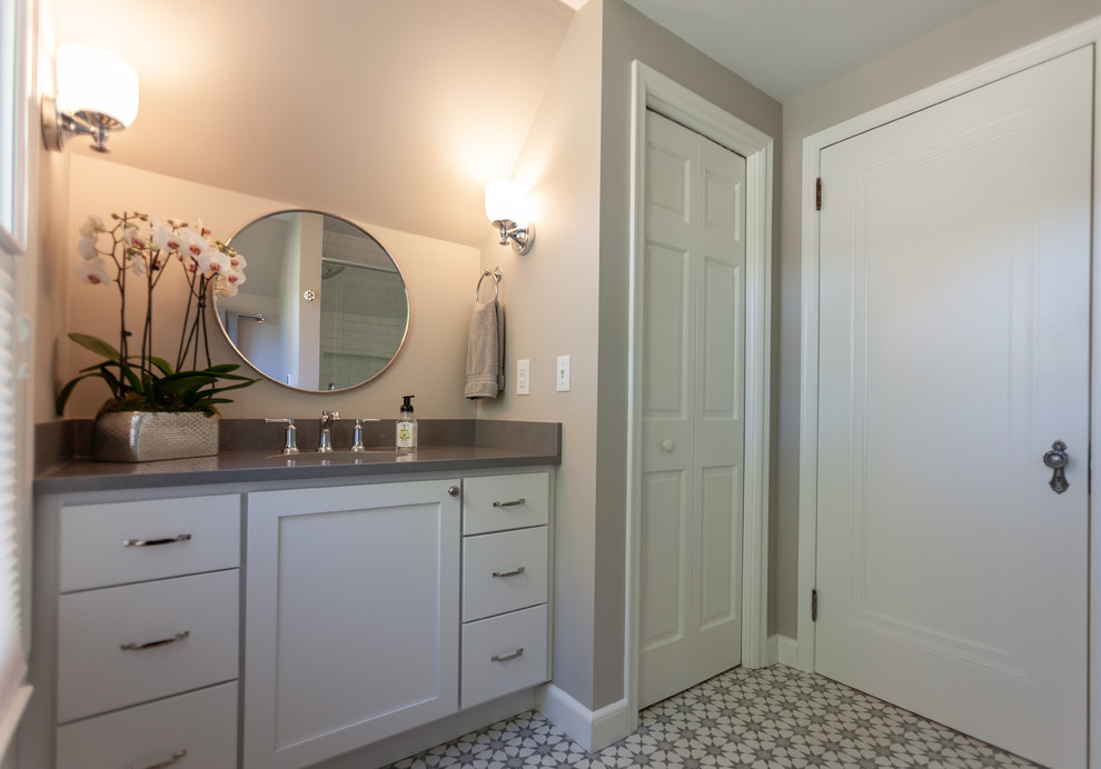 Bild på ett mellanstort vintage grå grått badrum med dusch, med luckor med infälld panel, vita skåp, en dusch i en alkov, en toalettstol med hel cisternkåpa, grå väggar, cementgolv, ett undermonterad handfat, bänkskiva i kvarts, flerfärgat golv och dusch med gångjärnsdörr