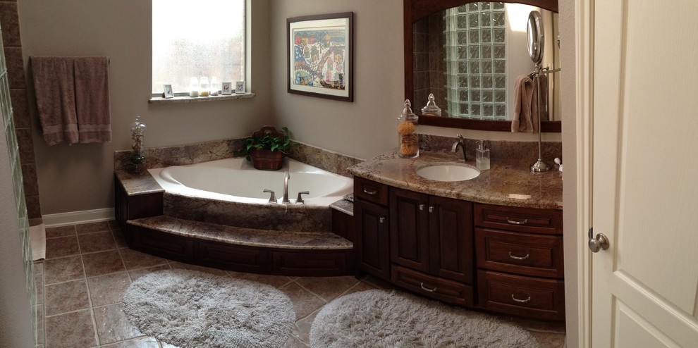Photo of a medium sized classic ensuite bathroom in Houston with raised-panel cabinets, dark wood cabinets, a corner bath, a built-in shower, beige tiles, brown tiles, stone slabs, beige walls, ceramic flooring, a submerged sink and granite worktops.