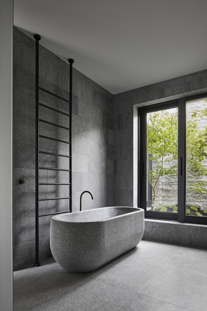 Photo of a modern grey and black bathroom with a freestanding bath, grey tiles, grey walls and grey floors.