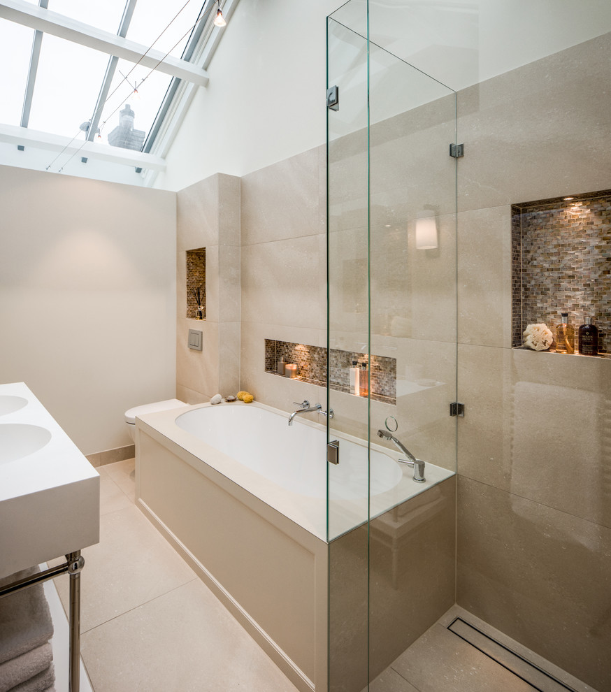Cette image montre une salle de bain principale design avec un placard sans porte, une baignoire encastrée, une douche d'angle, un carrelage beige, un mur beige, un lavabo intégré, un sol beige, une cabine de douche à porte battante, une niche et un mur en pierre.