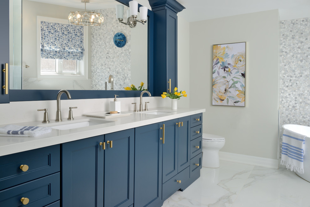 Design ideas for a large classic ensuite bathroom in Toronto with blue cabinets, a freestanding bath, white tiles, marble tiles, grey walls, ceramic flooring, engineered stone worktops, white floors, white worktops, recessed-panel cabinets and a submerged sink.