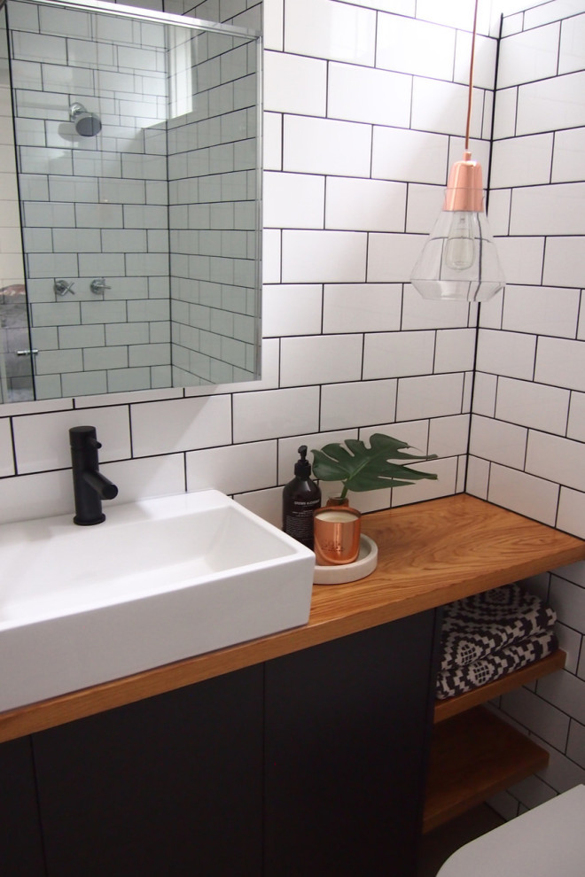 Modern inredning av ett litet beige beige badrum med dusch, med släta luckor, grå skåp, en hörndusch, en toalettstol med hel cisternkåpa, vit kakel, keramikplattor, vita väggar, klinkergolv i keramik, ett avlångt handfat, träbänkskiva, beiget golv och dusch med gångjärnsdörr