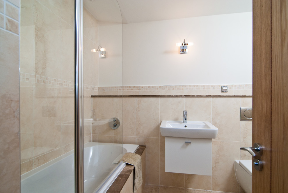 Ejemplo de cuarto de baño principal actual pequeño con lavabo suspendido, armarios tipo mueble, puertas de armario blancas, bañera empotrada, ducha empotrada, sanitario de pared y baldosas y/o azulejos beige