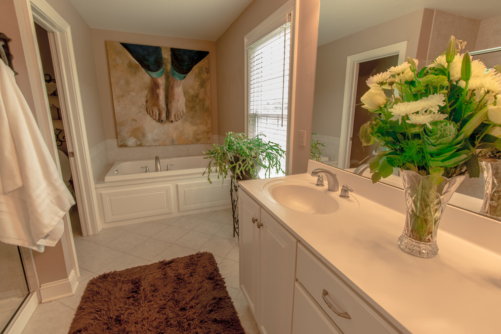 Klassisk inredning av ett stort en-suite badrum, med ett integrerad handfat, luckor med upphöjd panel, vita skåp, bänkskiva i akrylsten, ett platsbyggt badkar, en hörndusch, beige kakel, porslinskakel, beige väggar och klinkergolv i porslin