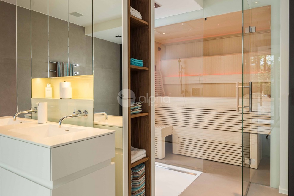 Inspiration for an expansive contemporary sauna bathroom in New York with freestanding cabinets, white cabinets, a freestanding bath, a walk-in shower, an integrated sink, an open shower, a wall mounted toilet, beige tiles, stone tiles, beige walls, travertine flooring, engineered stone worktops, grey floors and white worktops.