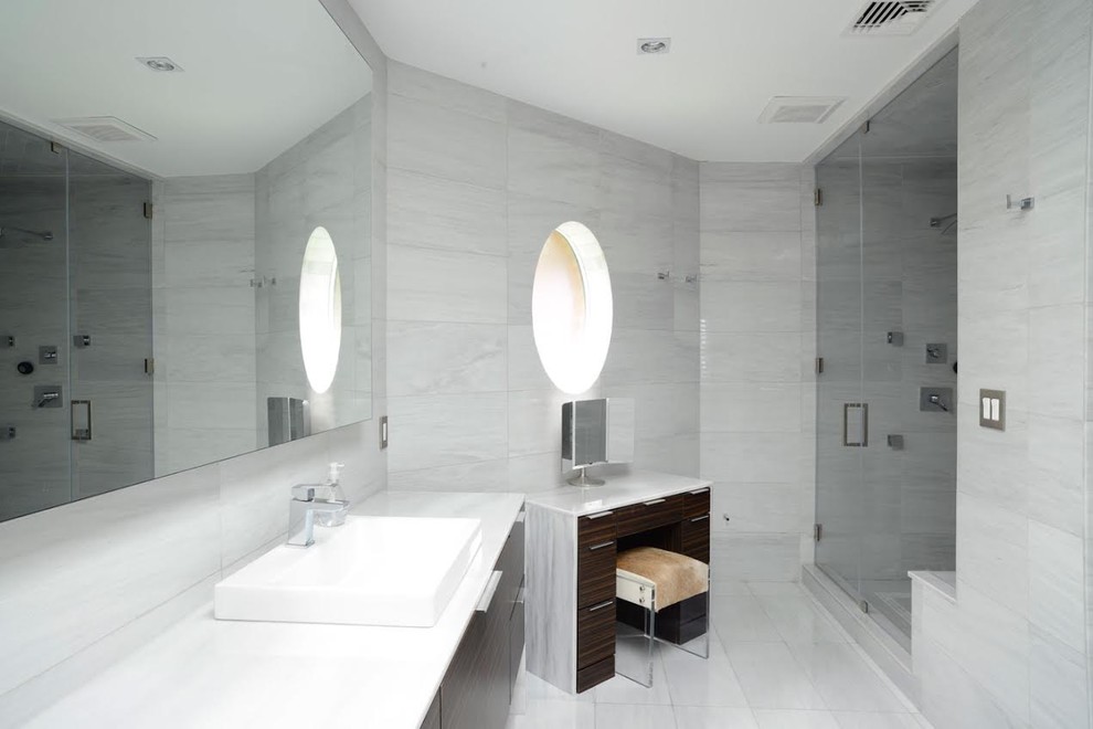 На фото: большая главная ванная комната в стиле модернизм с плоскими фасадами, темными деревянными фасадами, отдельно стоящей ванной, душем в нише, серой плиткой, мраморной плиткой, серыми стенами, мраморным полом, настольной раковиной, столешницей из искусственного камня, серым полом, душем с распашными дверями и белой столешницей с