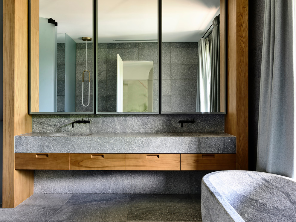 Modernes Badezimmer mit flächenbündigen Schrankfronten, hellbraunen Holzschränken, freistehender Badewanne, grauen Fliesen, grauer Wandfarbe, integriertem Waschbecken, grauem Boden und grauer Waschtischplatte