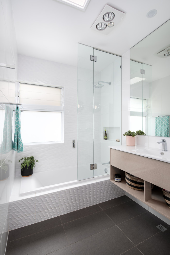 Modernes Badezimmer mit flächenbündigen Schrankfronten, hellen Holzschränken, Einbaubadewanne, weißen Fliesen, integriertem Waschbecken, grauem Boden, weißer Waschtischplatte, Einzelwaschbecken und schwebendem Waschtisch in Brisbane