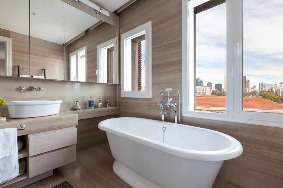 マドリードにある広いトランジショナルスタイルのおしゃれなマスターバスルーム (フラットパネル扉のキャビネット、淡色木目調キャビネット、置き型浴槽、シャワー付き浴槽	、ベッセル式洗面器、茶色いタイル) の写真