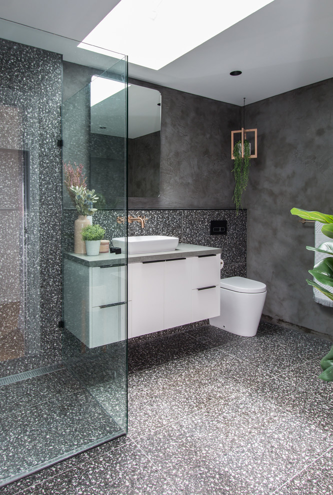 Cette photo montre une salle d'eau tendance avec un placard à porte plane, des portes de placard blanches, une douche d'angle, WC à poser, un carrelage gris, un mur gris, une vasque, un sol gris et un plan de toilette gris.