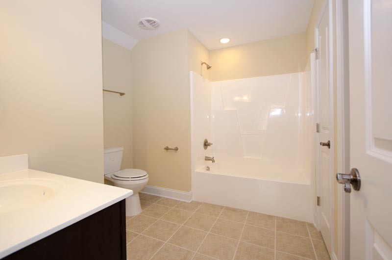 Modern inredning av ett badrum, med ett integrerad handfat, skåp i mörkt trä, en dusch/badkar-kombination och en toalettstol med separat cisternkåpa