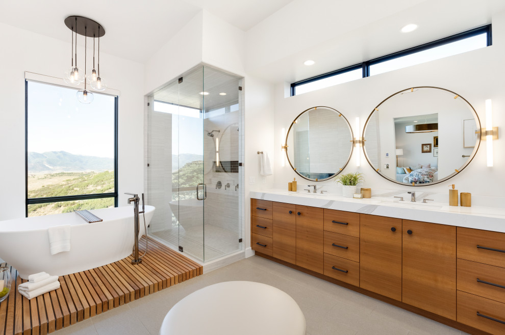 На фото: ванная комната в современном стиле с плоскими фасадами, фасадами цвета дерева среднего тона, отдельно стоящей ванной, угловым душем, белыми стенами, врезной раковиной, серым полом, душем с распашными дверями и белой столешницей