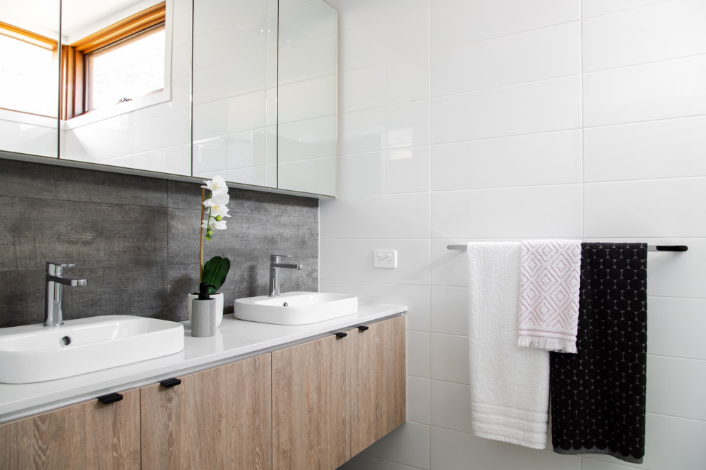 Réalisation d'une salle de bain design en bois brun avec un placard à porte plane, un carrelage blanc, une vasque, un plan de toilette blanc, meuble double vasque et meuble-lavabo suspendu.