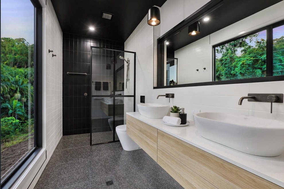 Diseño de cuarto de baño contemporáneo con armarios con paneles lisos, puertas de armario de madera clara, ducha a ras de suelo, baldosas y/o azulejos blancos, paredes blancas, lavabo sobreencimera, suelo gris, ducha abierta y encimeras blancas
