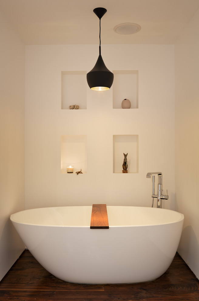 Bild på ett funkis badrum, med ett fristående badkar, vita väggar och mörkt trägolv