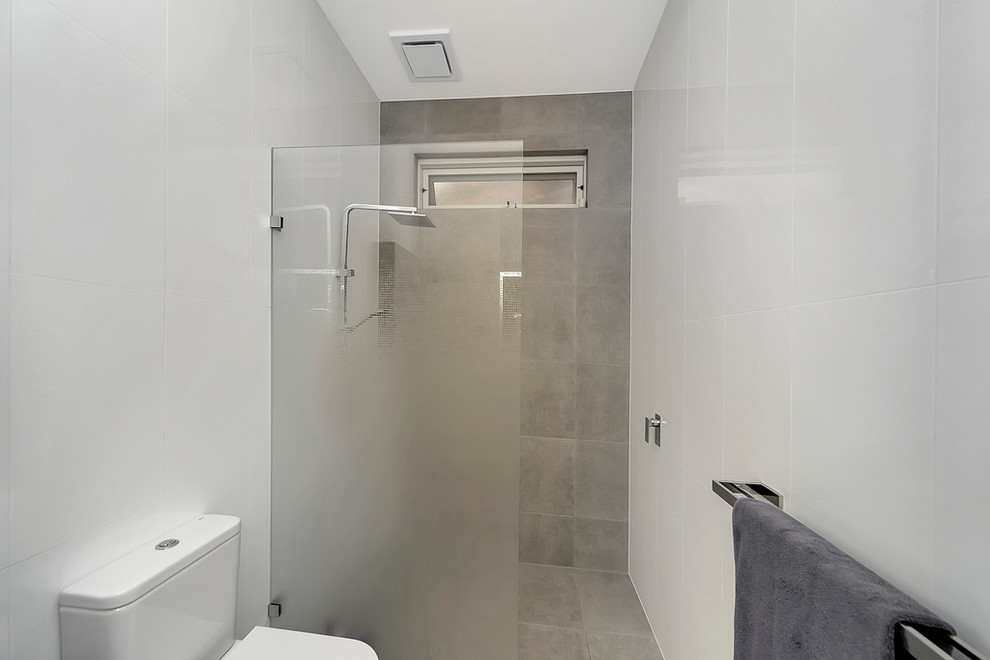 Bild på ett funkis badrum, med släta luckor, skåp i mellenmörkt trä, en dusch i en alkov, en toalettstol med separat cisternkåpa, grå kakel, vit kakel, cementkakel, grå väggar, cementgolv, ett integrerad handfat, bänkskiva i kvarts, grått golv och med dusch som är öppen