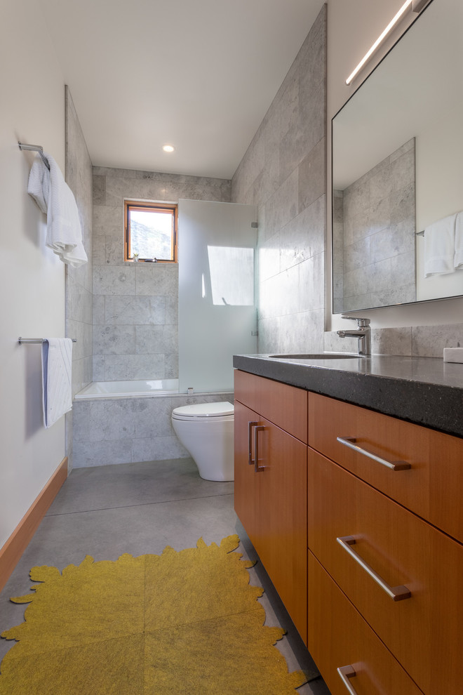Inspiration for a medium sized retro shower room bathroom in Seattle with flat-panel cabinets, medium wood cabinets, an alcove bath, a shower/bath combination, a two-piece toilet, grey tiles, marble tiles, white walls, concrete flooring, a submerged sink, engineered stone worktops, grey floors, an open shower and grey worktops.